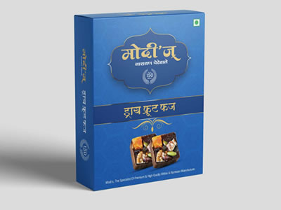 A blue rectangular box of Drt Fruit Fudge with premium gold and white Hindi-English text, decorative designs, chikki images at the bottom front, and a small green square in the corner. The pack size is 500 grams.