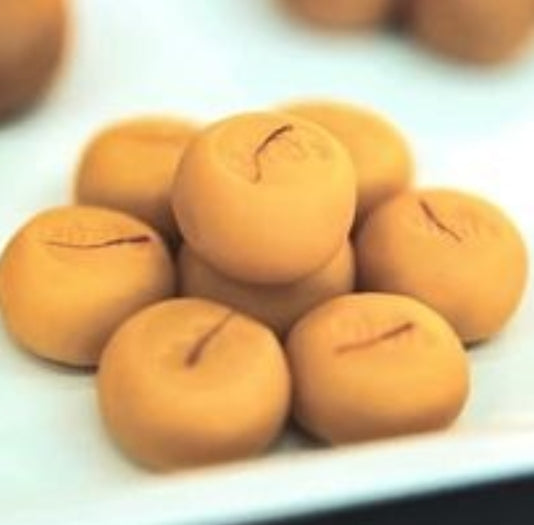 A close-up of a stack of round, golden-brown Kesar Pedha topped with saffron strands, arranged on a white plate—a tempting sweet treat from the Summer Combo @ 599 by MS Bytes.