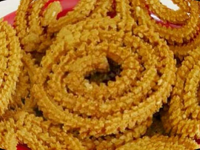 A close-up of golden-brown, spiral-shaped Chakli snacks arranged on a red plate—crunchy and perfect for snacking. Now available in 500g packs.