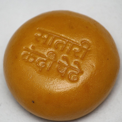 A close-up of the round, brown Satari Kandi Pedha with embossed Hindi text on top, placed on a white surface. This 400g pack is perfect for gifting and delivers authentic traditional flavor in every bite.